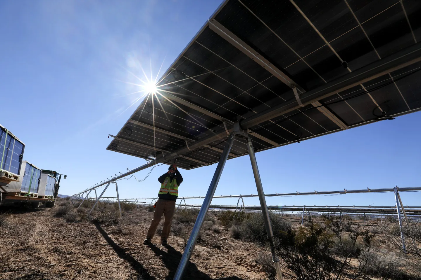 A worker is shown installing utility-scale solar panels in Nevada under the sun.